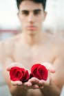Morena jovem sem camisa cara mostrando vinous rosas frescas e olhando para a câmera no fundo borrado — Fotografia de Stock