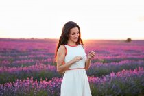 Smiling young woman showing flowers between violet lavender field — Stock Photo