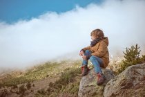 Menino sentado perto da colina no dia nebuloso — Fotografia de Stock