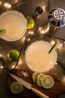 Verres de cocktail margarita sur table éclairée avec ingrédients — Photo de stock