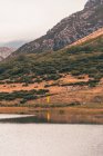 Persona in impermeabile giallo che va sulla riva del lago vicino a una montagna in Isoba, Castiglia e Leon, Spagna — Foto stock