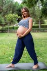 Smiling pregnant attractive woman training on mat in park — Stock Photo
