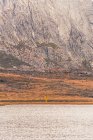 Persona en impermeable amarillo que va a la orilla del lago cerca de una montaña en Isoba, Castilla y León, España - foto de stock