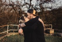 Вид збоку бородатий чоловік обіймає і цілує жінку в окулярах в парку на розмитому фоні — стокове фото