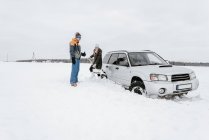 Young lady with shovel digging snow from automobile near guy in winter wear on meadow in Vilnius, Lithuania — Stock Photo