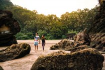 Вид на молодую пару между скалами на песчаном пляже возле зеленого тропического леса в Малайзии — стоковое фото