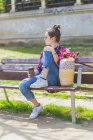 Vue latérale d'une jeune femme hipster assise sur un banc de parc se détendre par une journée ensoleillée tout en regardant loin — Photo de stock