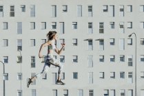 Женщина в спортивной одежде прыгает рядом со зданием — стоковое фото