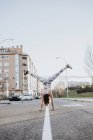 Visão traseira da jovem mulher em sportswear fazendo suporte de mão na estrada de asfalto na cidade — Fotografia de Stock
