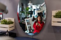 Вид збоку весела дама тримає мобільний телефон і сушильні волоски в перукарні — стокове фото