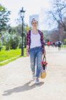 Frontansicht einer jungen lächelnden Hipsterfrau, die an sonnigen Tagen in einem Park spaziert und dabei einen bösen Korb hält — Stockfoto