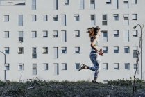 Женщина в спортивной одежде бежит возле здания — стоковое фото