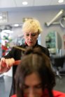 Aged stylist making hairdo to attractive young lady in hairdressing salon — Stock Photo
