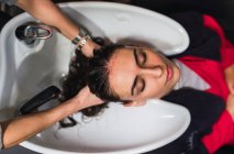 From above woman washing hairs to attractive lady with closed eyes in sink — Stock Photo