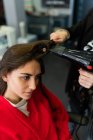 Стилист урожая, использующий фен и расческу и делающий прическу привлекательной женщине в парикмахерской — стоковое фото
