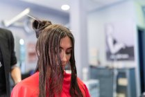 У віці стиліст робить зачіску для привабливої молодої леді в перукарні — стокове фото