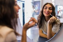 Reflection of young beautiful lady with hand near lips looking at mirror in hairdressing salon — Stock Photo