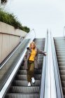 Blonde girl going down escalators in shopping center — Stock Photo