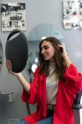 Stylist hält Spiegel mit Reflexion der attraktiven, fröhlichen Dame im Friseursalon — Stockfoto