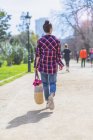 Vista posteriore di una giovane hipster che cammina in un parco nella giornata di sole mentre tiene in mano un cesto malvagio — Foto stock