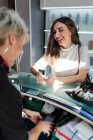 Вид збоку щасливої леді з макіяжем, що платить пластиковою карткою біля веселого стиліста в перукарні — стокове фото