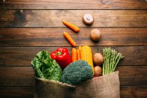 Assortiment de légumes crus frais avec sac sur table de cuisine en bois — Photo de stock