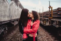 Hombre de pelo largo abrazando y besando a mujer cerca del tren - foto de stock