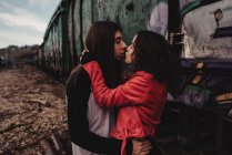 Длинноволосый мужчина обнимает и целует женщину возле поезда — стоковое фото