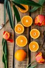 Зверху красиві тюльпани і свіжі апельсини на поверхні пиломатеріалу біля ножа і листя рослини . — стокове фото