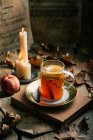 Чашка свежего чая с лимоном рядом с спелым яблоком и пылающими свечами среди осенних листьев . — стоковое фото