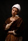Medieval young maid holding flower on black background. — Stock Photo