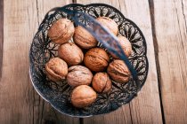 From above ornamental metal basket with fresh walnuts placed on wooden tabletop. — Stock Photo