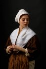 Mujer bonita en ropa medieval simple con los ojos cerrados sobre fondo negro . - foto de stock