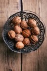 From above ornamental metal basket with fresh walnuts placed on wooden tabletop. — Stock Photo
