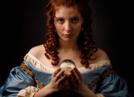 Schöne Frau im eleganten mittelalterlichen Kleid mit Glaskugel und Blick in die Kamera. — Stockfoto