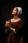Medieval maid with glass of milk on black background. — Stock Photo