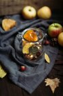 Small nuts and dried autumn leaves placed in glass jar with fairy lights on piece of fabric near fresh apples. — Stock Photo
