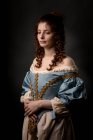 Atractiva joven dama en hermoso vestido barroco con las manos en el vientre sobre fondo negro . - foto de stock