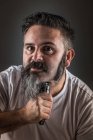 Парикмахер бреет бороду и смотрит в камеру — стоковое фото