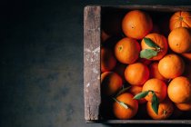 Frische Orangen in alter Holzkiste auf dunklem Hintergrund — Stockfoto