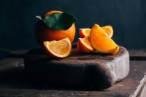 Oranges fraîches entières et coupées sur fond bois foncé — Photo de stock