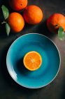 Mitad naranja fresca en plato azul sobre fondo oscuro con frutas enteras - foto de stock
