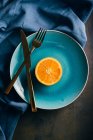 Frische orangefarbene Hälfte in blauem Teller auf dunklem Hintergrund mit Stoff und Besteck — Stockfoto