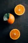 Naranjas cortadas a la mitad y enteras sobre fondo oscuro - foto de stock