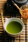 Nahaufnahme der Tasse mit frischem grünen Matcha-Tee, Vintage-Kanne und Bambusbesen Vorbereitungswerkzeug auf dem Tisch. — Stockfoto