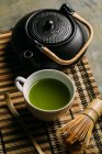 Primer plano de la taza con té matcha verde fresco, olla vintage y batidor de bambú herramienta de preparación en la mesa . - foto de stock