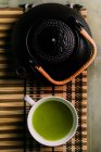 Nahaufnahme der Tasse mit frischem grünen Matcha-Tee, Vintage-Kanne und Bambusbesen Vorbereitungswerkzeug auf dem Tisch. — Stockfoto