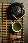 Close-up of cup with fresh green matcha tea, vintage pot and bamboo whisk preparing tool on table. — Stock Photo
