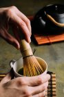 Close-up de mãos de pessoa preparando chá matcha com batedor de bambu . — Fotografia de Stock