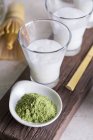 Glasses of milk and matcha powder, process of preparing matcha latte beverage. — Stock Photo